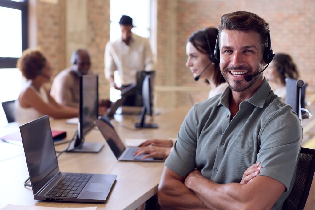 Businessman In Multi-Cultural Business Team Wearing Headsets In Customer Support Centre